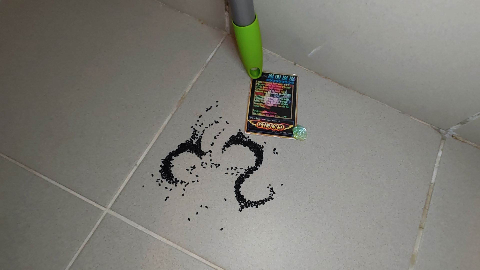 foto of a dust cleaner tip holding a Yu-Gi-Oh card with some black sesame seeds and a small pastic rose