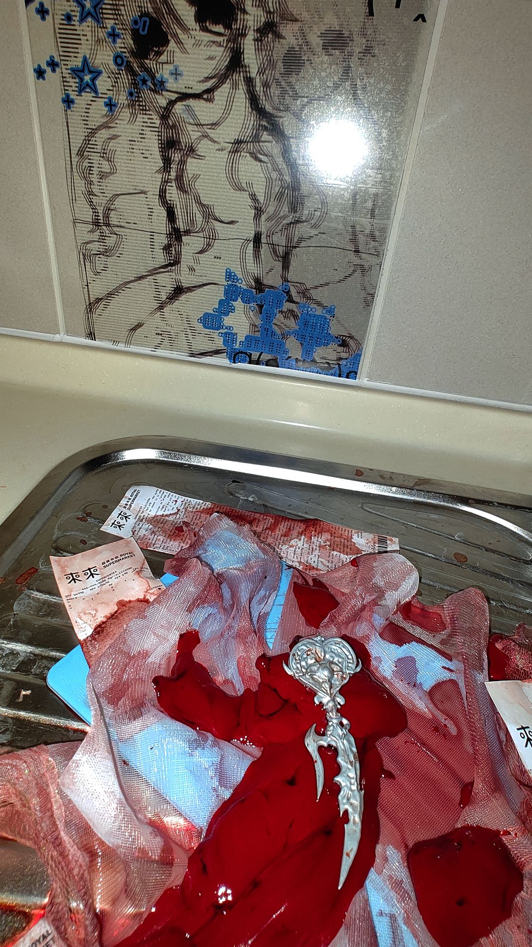 image of the silver heart wand laying on red liver in the silver sink and picture of a waifu with blue stars that match the blue cutting board bellow the wand, lace and liver.