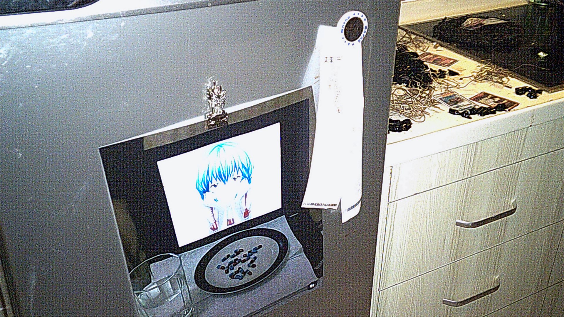 close up of picture of Rei from the anime series Neon Genesis Evangelion. its an image of her in a pc screen with a plate full of red and blue pills and a glass of water. this image is holded by a kitchen magnet in the fridge'. there's another magnet holding supermarket receipts